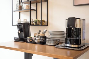Una estación de café con cafetera, dispensador de agua y una bandeja con tazas y cubiertos.