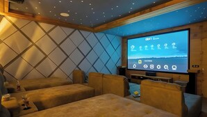 A cozy room with a large screen displaying a weather app, plush seating, and a wooden ceiling. - amã Stays & Trails Kedar Villa, Mukteshwar (Mukteshwar)