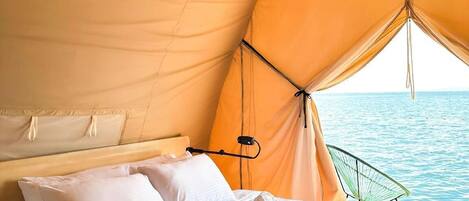 A tented room with a bed, pillows, and a view of the sea.
