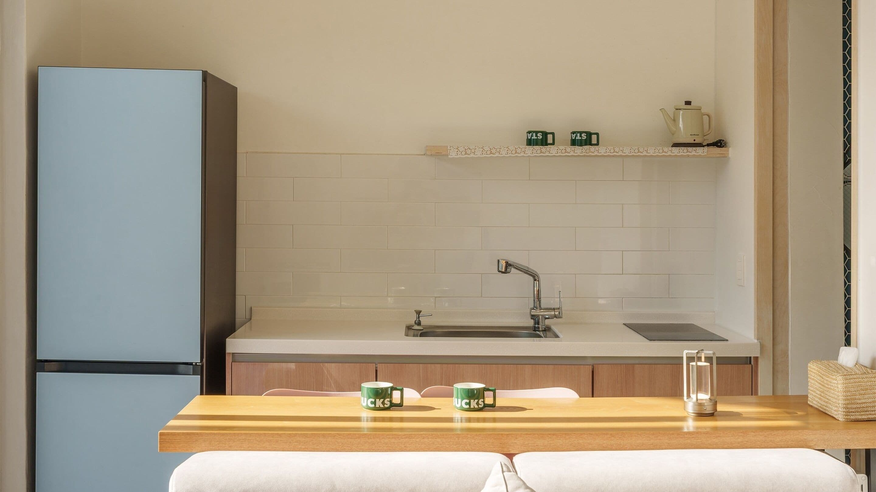 A modern kitchen with a built-in sink, a refrigerator, and a wooden table with two mugs.