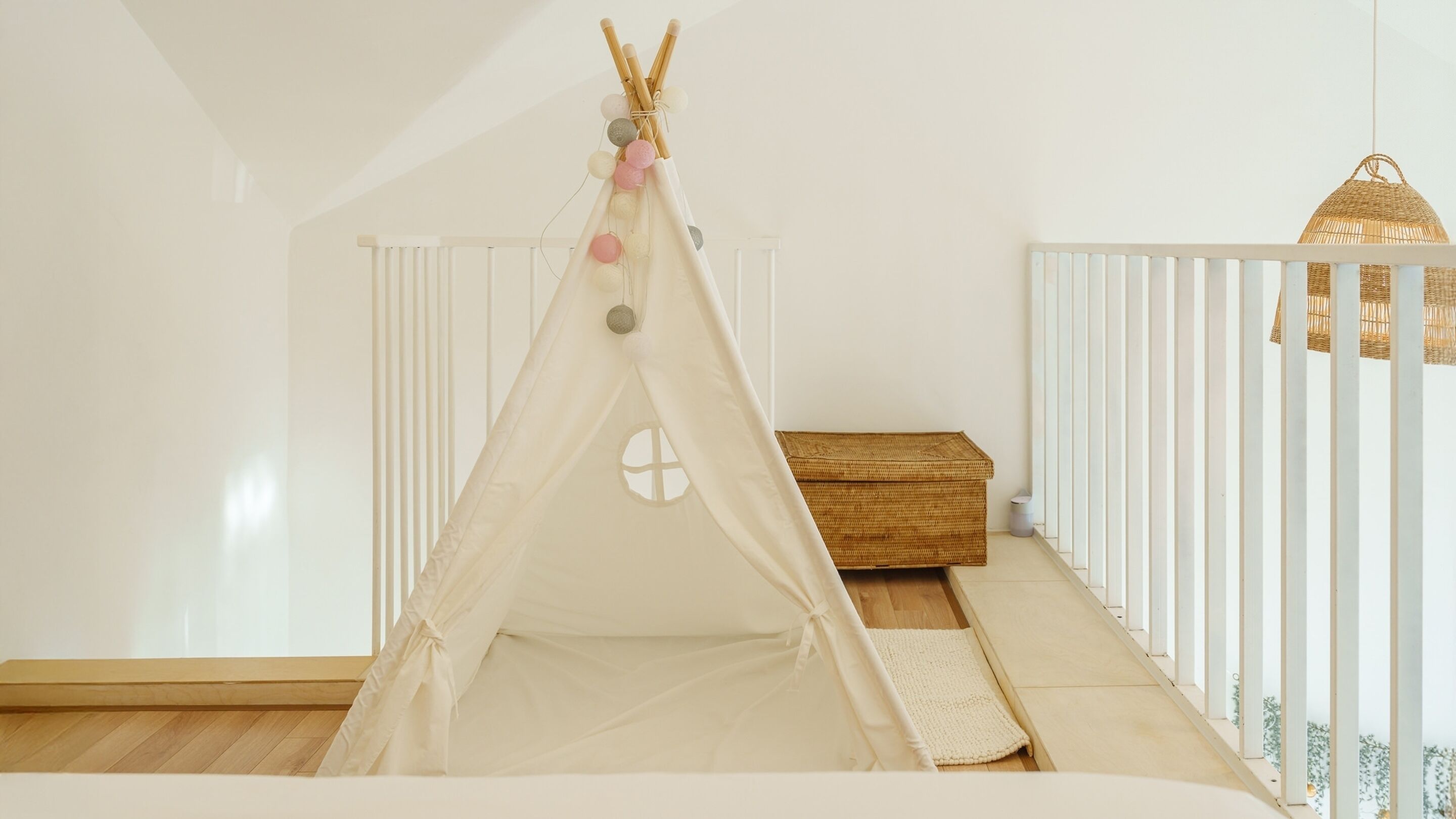 A cozy room with a white crib, a white crib rail, a woven basket, and a hanging light fixture.