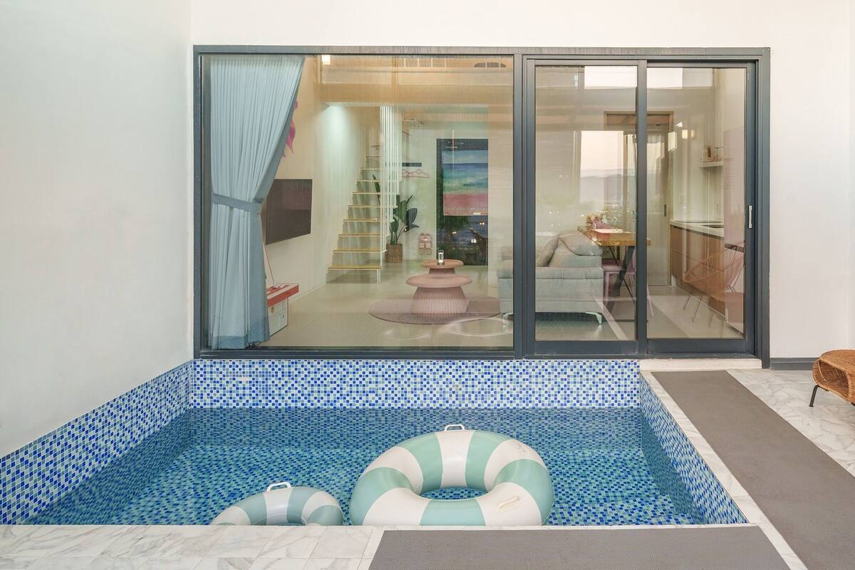 Ein modernes Hallenbad mit großen Glaswänden, gefliestem Boden und zwei Liegestühlen.
