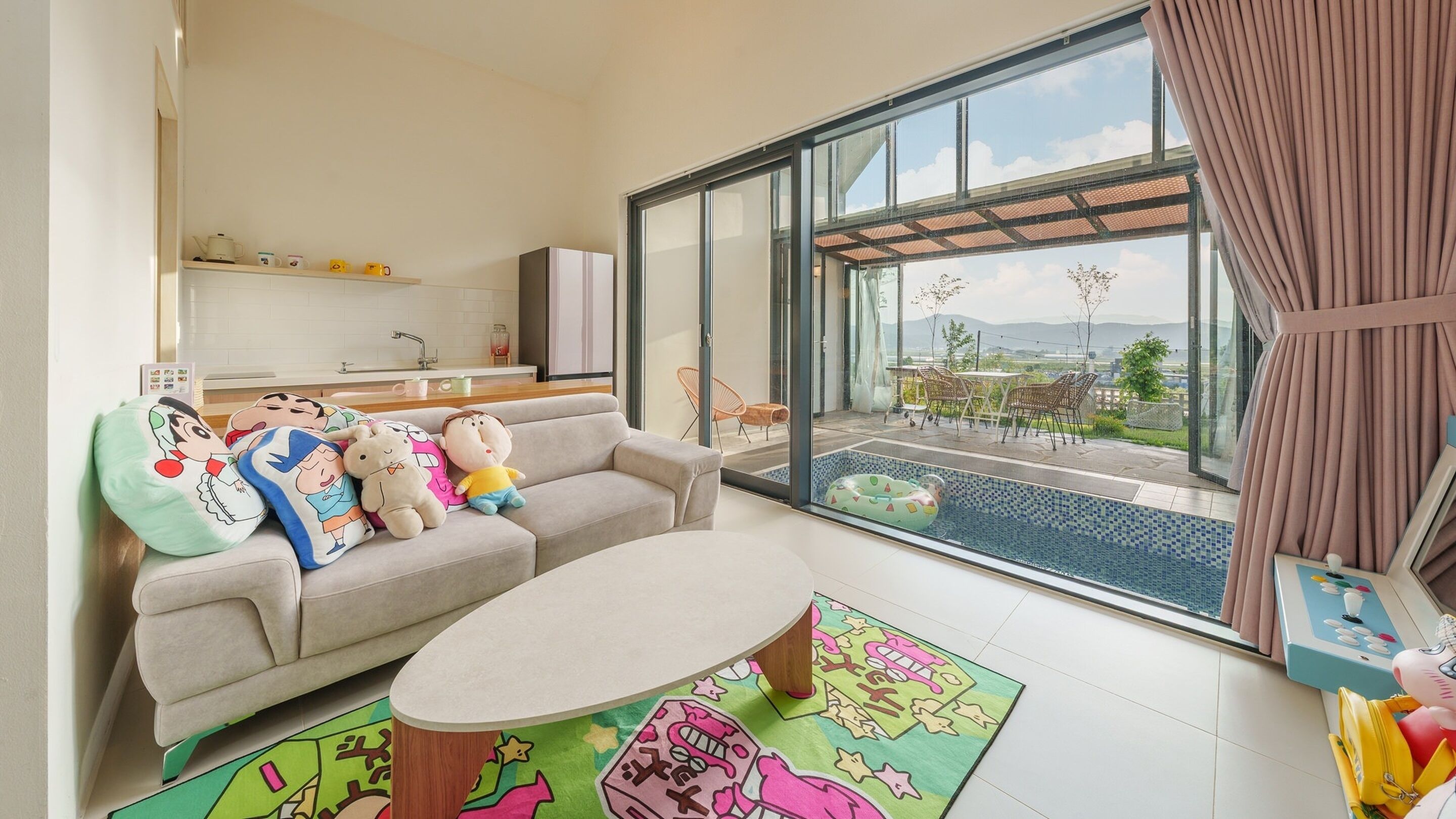 Una sala de estar moderna con un sofá, alfombras coloridas, una mesa de comedor y vistas a una piscina y un área de estar al aire libre.