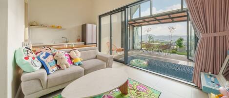 Una sala de estar moderna con un sofá, alfombras coloridas, una mesa de comedor y vistas a una piscina y un área de estar al aire libre.