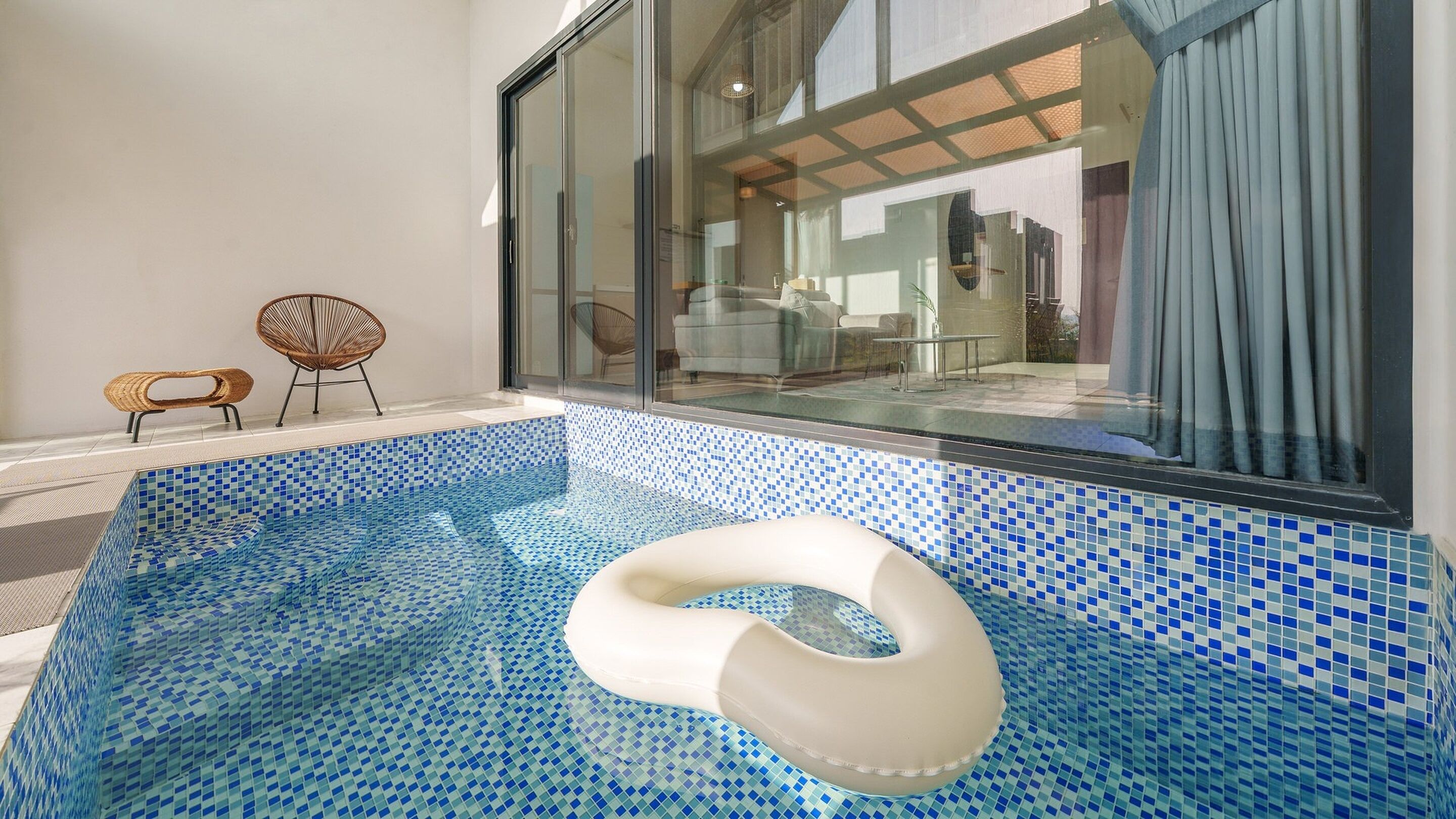Ein modernes Hallenbad mit blauen Mosaikfliesen, einem Liegestuhl und einem gläsernen Bereich mit Blick auf die Stadt.