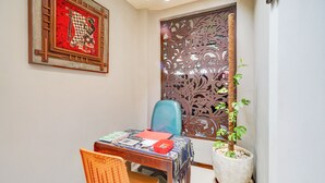 A room with a wooden table, a blue chair, a potted plant, and a decorative screen. - Hotel O Sidomulyo Heritage (Mojokerto)