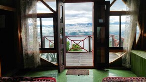 A room with a large open door leading to a balcony with a red railing, offering a view of the sky and distant landscape. - Rock Paradise Resort (Sajek)
