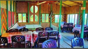 A dining area with tables and chairs, a wooden ceiling, and large windows. - Rock Paradise Resort (Sajek)