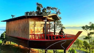 Eine bootförmige Holzhütte mit Balkon, gelegen an einem Hügel mit Blick auf die Landschaft.