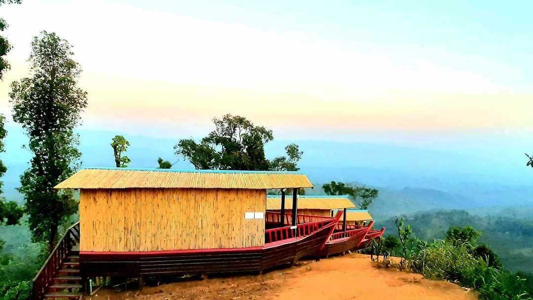 A bamboo structure with a staircase leading up, surrounded by greenery and a view of the landscape.