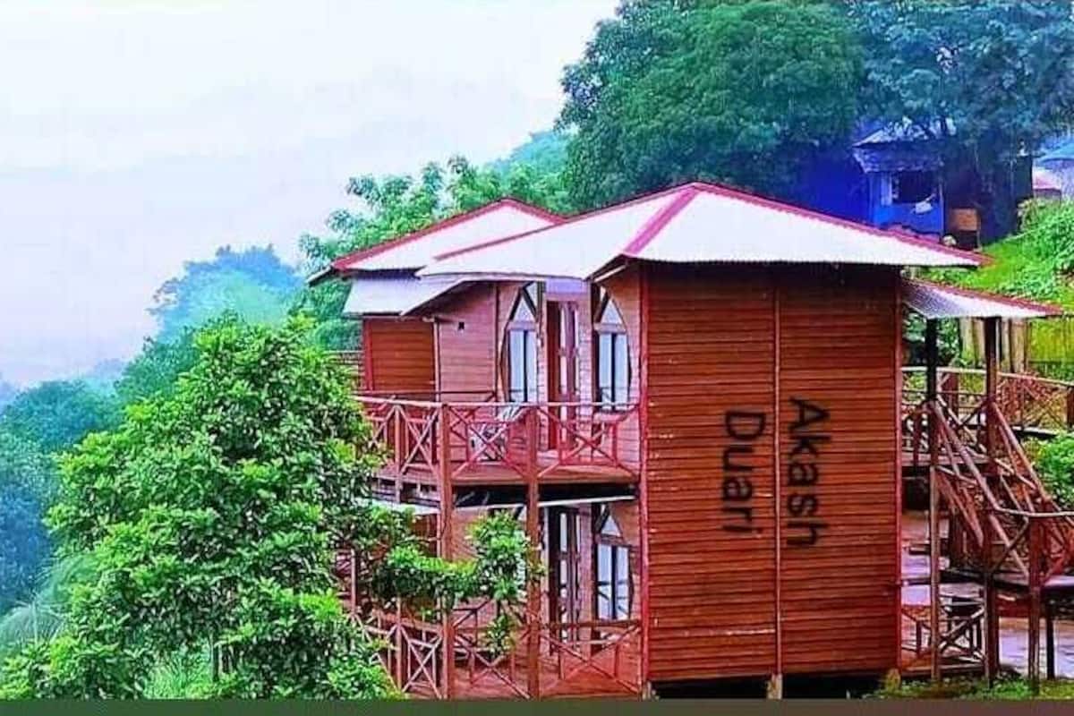A wooden building with a balcony, named 'Akash Duar', surrounded by lush greenery and mountains.