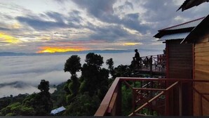 A wooden structure with a balcony overlooking a forested landscape and a sunset. - Rock Paradise Resort (Sajek)