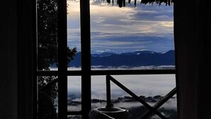 A view through a window with a metal railing, overlooking a mountainous landscape with a cloudy sky. - Rock Paradise Resort (Sajek)