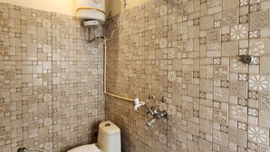 A bathroom with patterned tiles, a toilet, a shower, and a blue bucket. - Hotel Step Inn Gold (New Delhi)