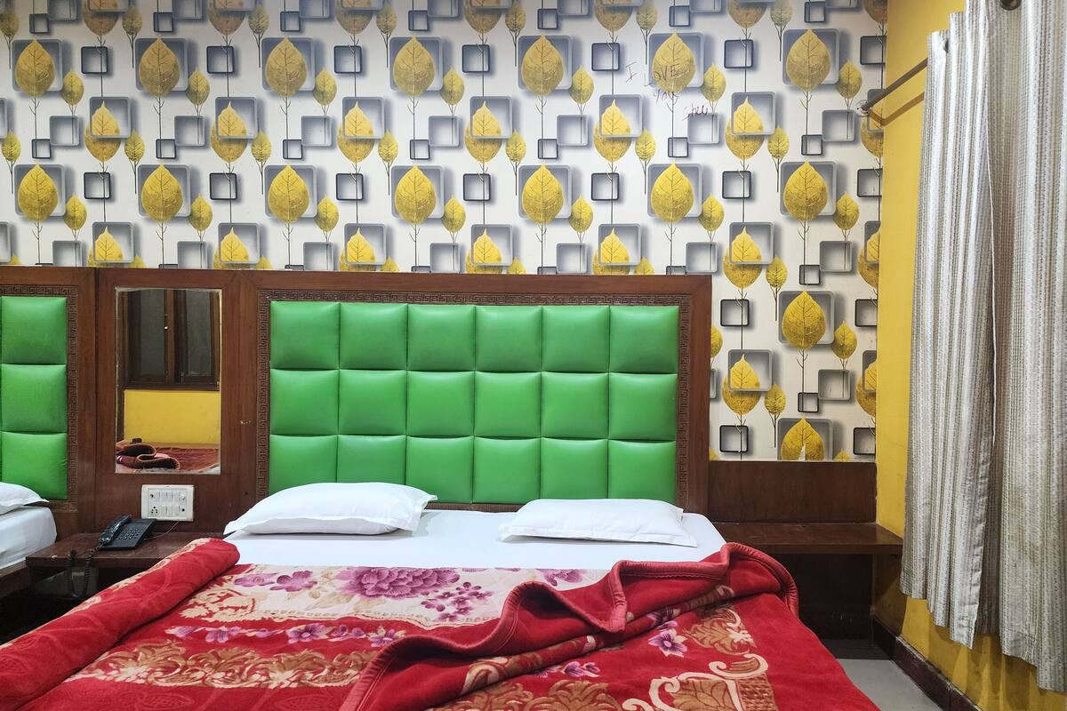 A hotel room with a green upholstered headboard, a floral-patterned bedspread, and a wall decorated with leaf motifs.