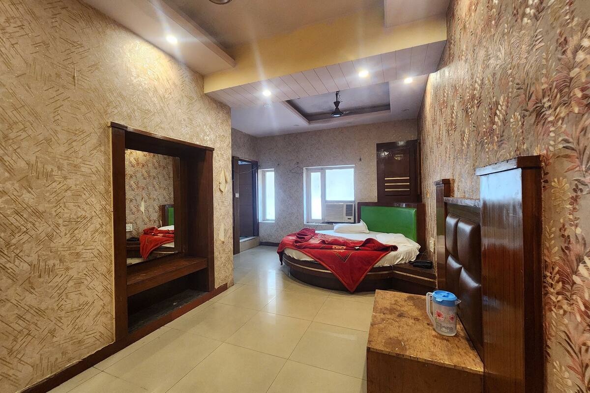 A hotel room with a bed, a wooden headboard, a mirror, a window, and a small table with a container.