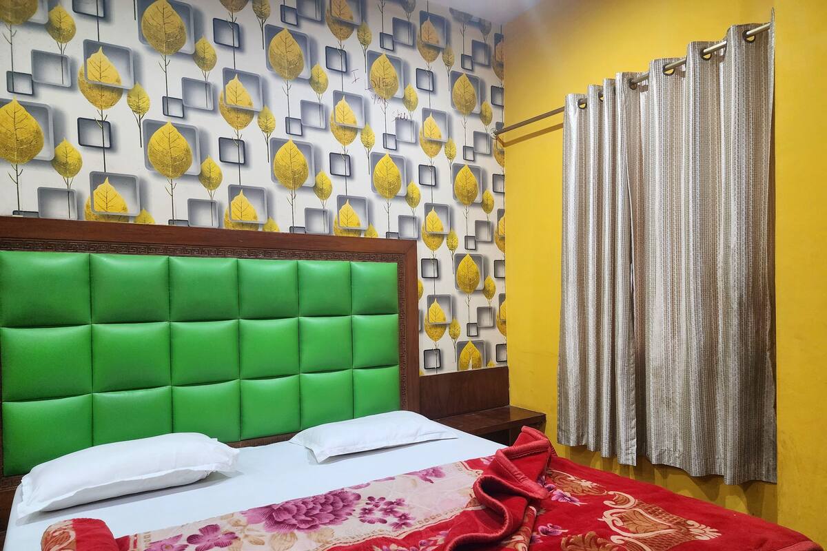 A hotel room with a green upholstered headboard, a floral-patterned bedspread, and a wall with a leaf-pattern wallpaper.