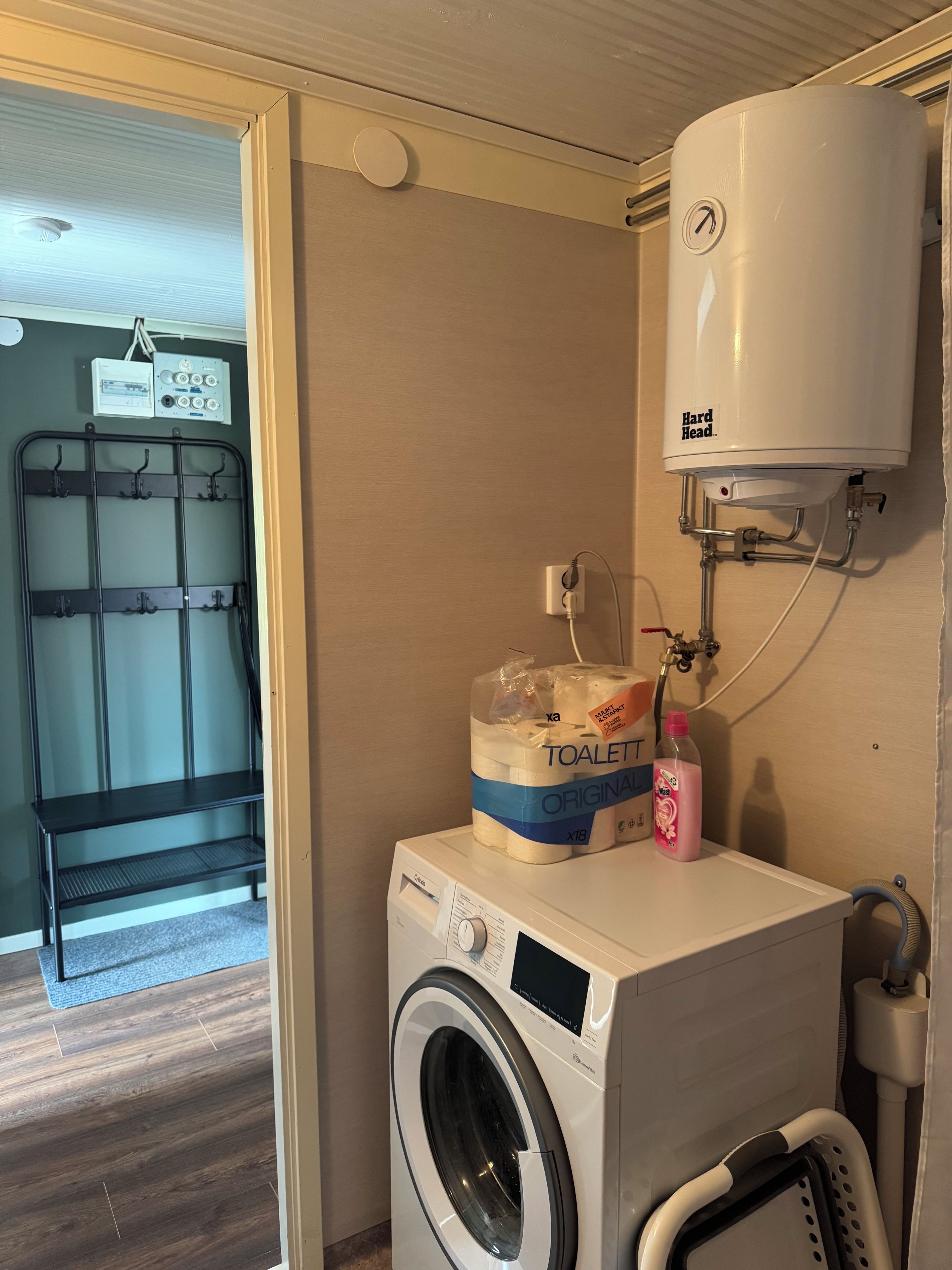 Un área de lavandería con lavadora, dispensador de papel higiénico y calentador de agua.