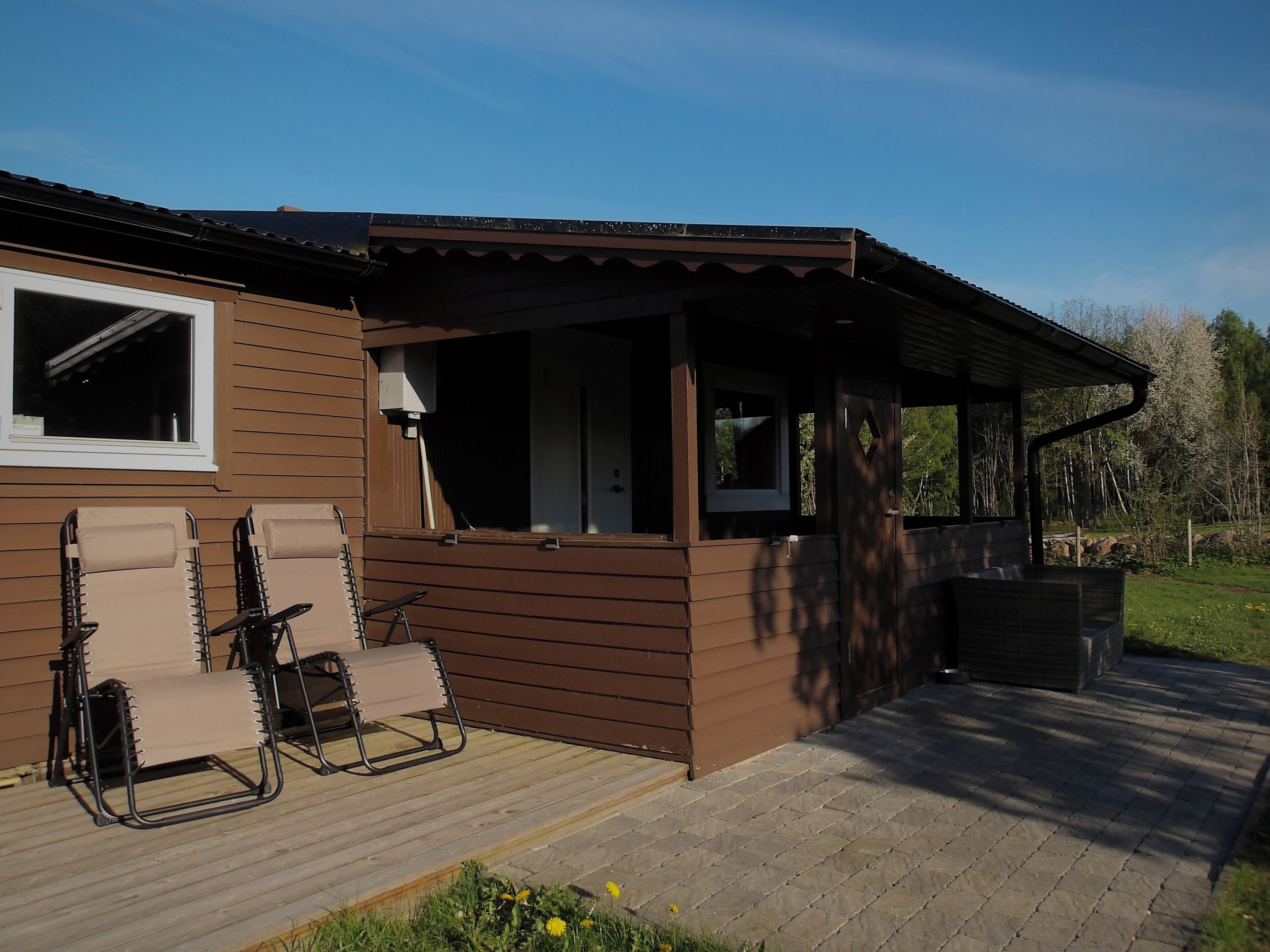 Une cabane en bois avec un porche couvert, deux chaises pliantes et une fenêtre.