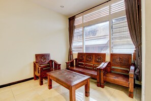 A room with a wooden sofa set, a matching wooden table, and a window with curtains. - Hotel O Mataram Residence (Semarang)