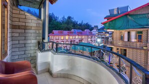 Un balcon doté d’une balustrade incurvée, une vue sur un immeuble avec de nombreuses fenêtres et, au loin, une zone boisée.