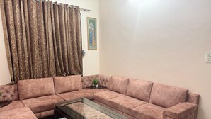 A living room with a sectional sofa, a glass coffee table, and a potted plant. - comfort castle (Jalandhar)