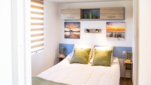 Een slaapkamer met een bed, twee nachtkastjes, een venster met jaloezieën en wandplanken met decoratieve objecten.