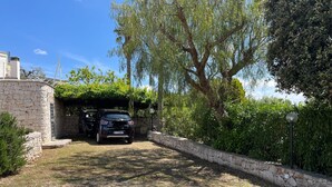 A gravel driveway leading to a covered parking area with a stone wall and greenery.