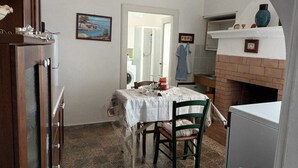 A compact kitchen with a dining table, chairs, a refrigerator, a brick fireplace, and a washing machine in the background.