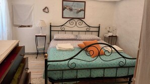 A bedroom with a metal bed frame, a bedside table with a lamp, a wall-mounted picture, and a window with a white curtain.