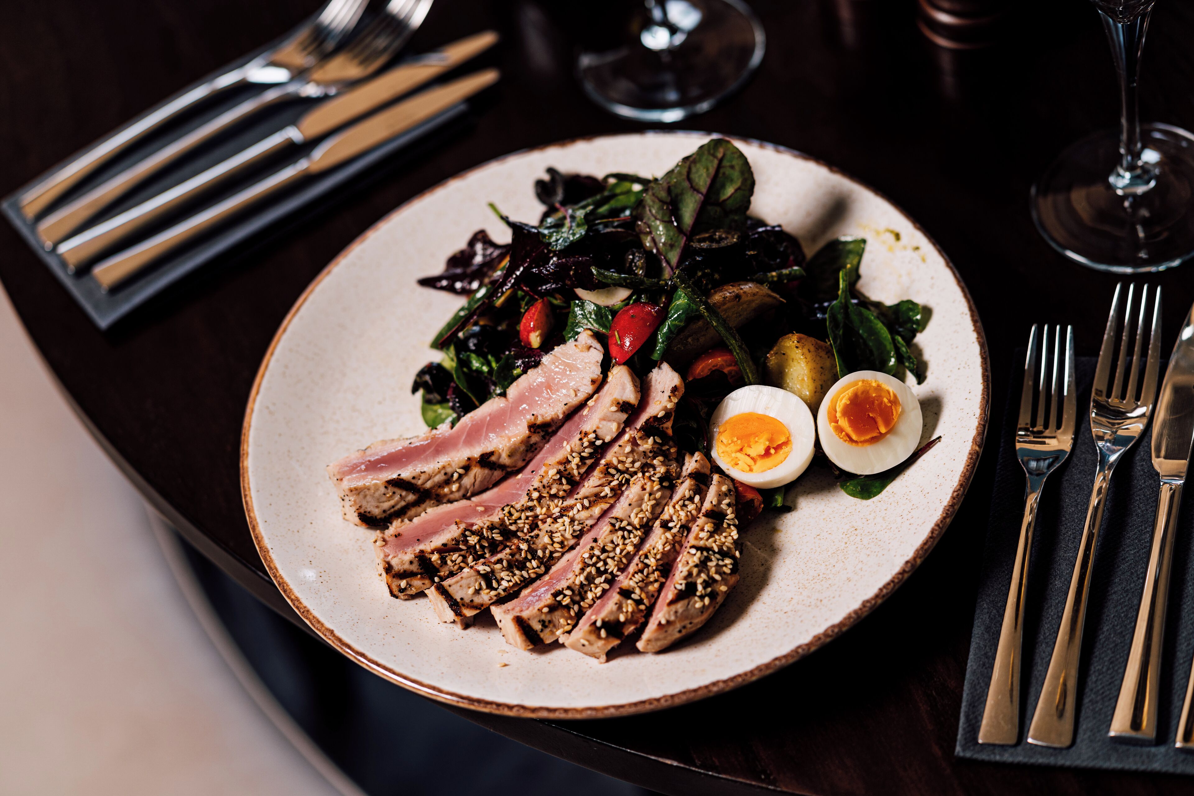 A plate with sliced meat, a boiled egg, and a salad on a ceramic plate.