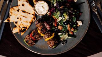 En tallerken med grillet frikadeller, ristede kartofler, pitabrød og en salat med feta.