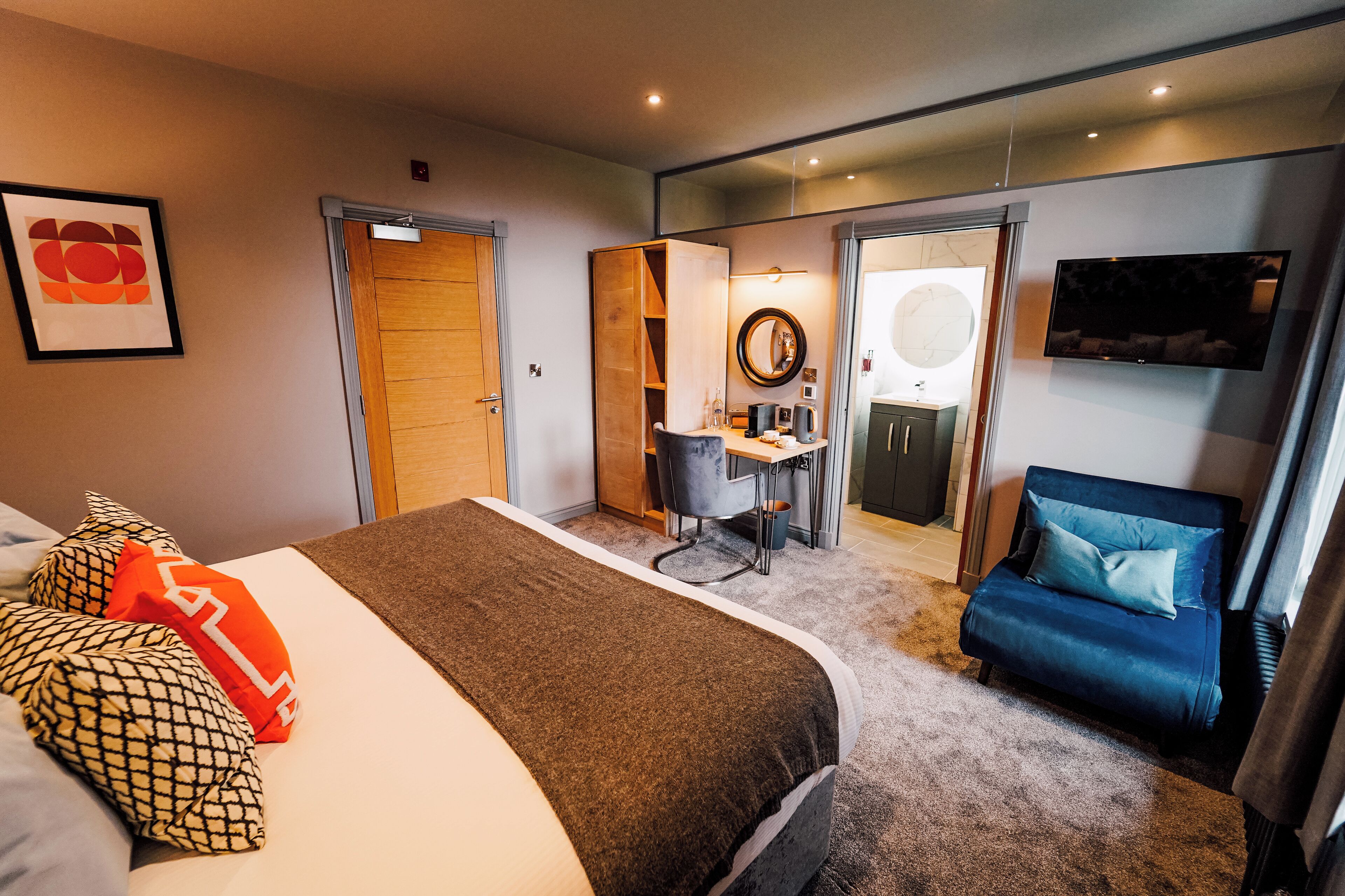 A hotel room with a bed, a desk, a chair, a TV, and a mirror.