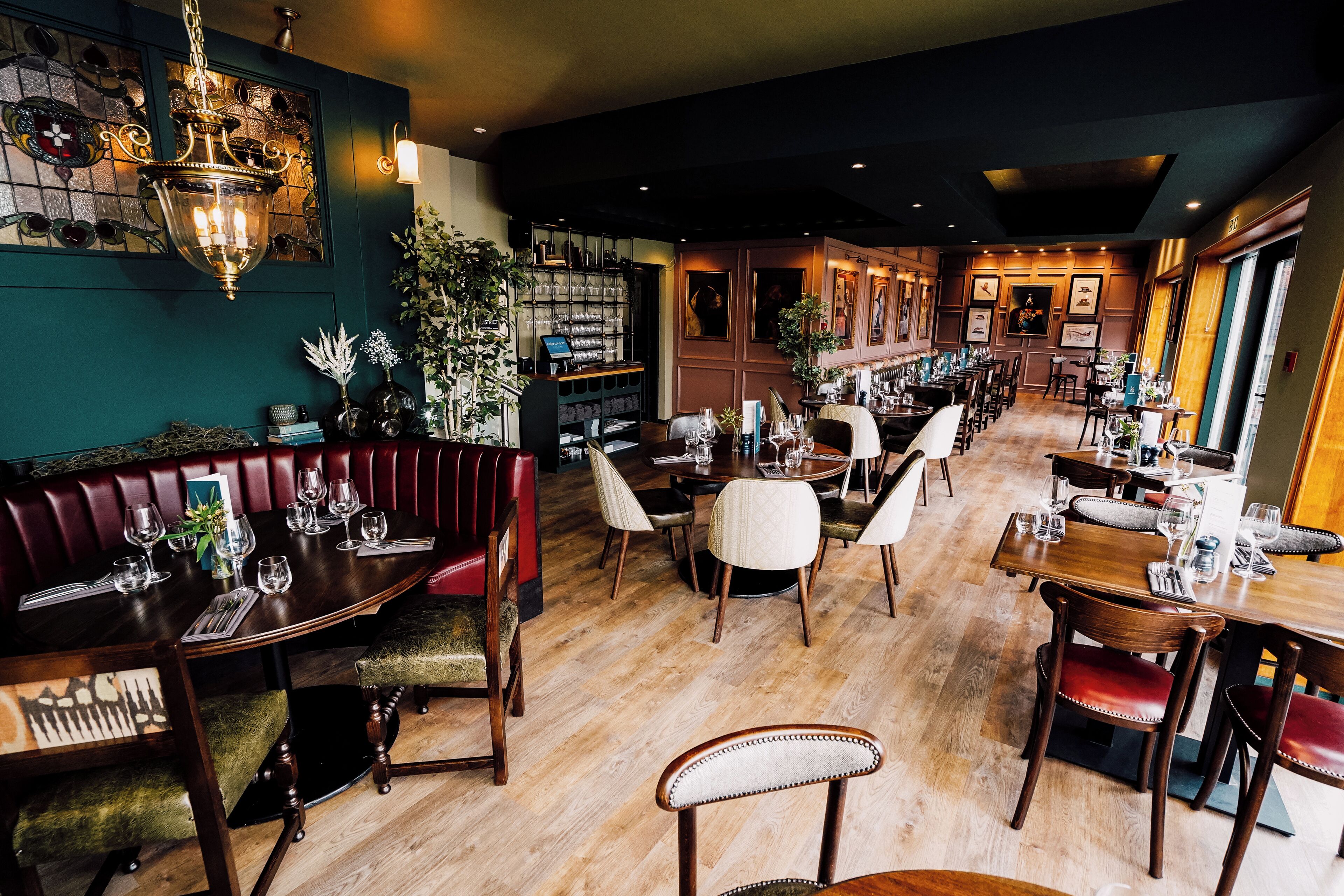 Een restaurant met houten tafels en stoelen, een bar en een groene wand met een kroonluchter.