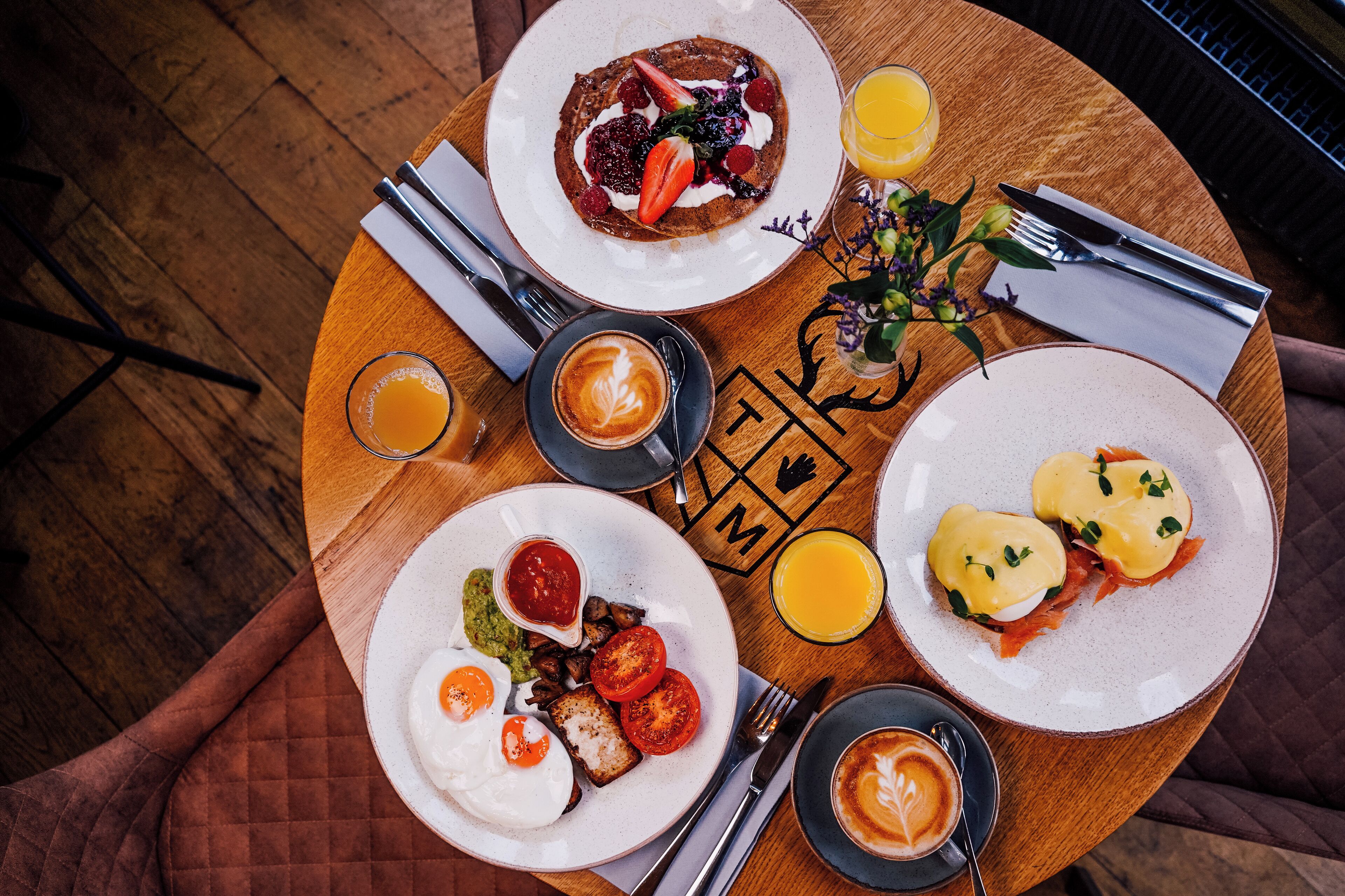 A breakfast setting with plates of eggs, toast, and pancakes, along with a cup of coffee and a glass of orange juice.