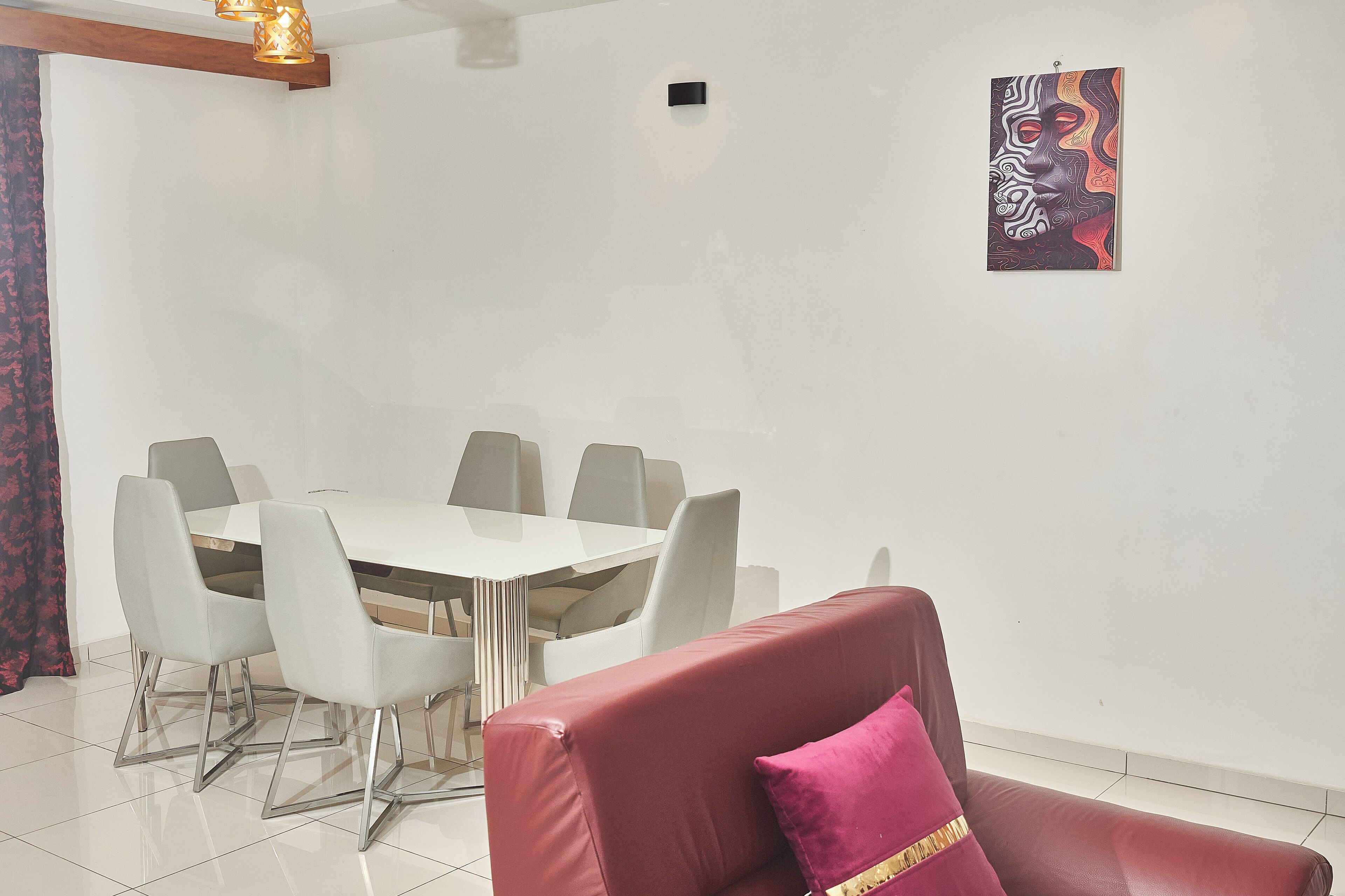 A dining area with a white table and chairs, a red sofa with a pink pillow, and a wall-mounted artwork.
