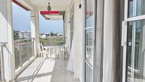 Een balkon met een tafel en stoelen, een hekwerk en een uitzicht op gebouwen in de verte.
