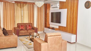 Een moderne woonkamer met een grote flatscreen televisie, leren banken, een glazen salontafel en een houten accentmuur.