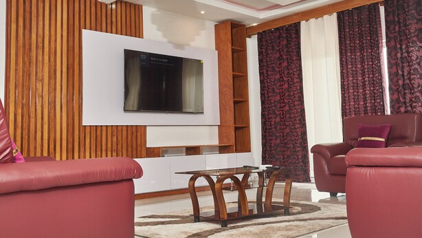 Een moderne woonkamer met een flatscreen televisie aan de muur, een wand van hout en rode leren banken.