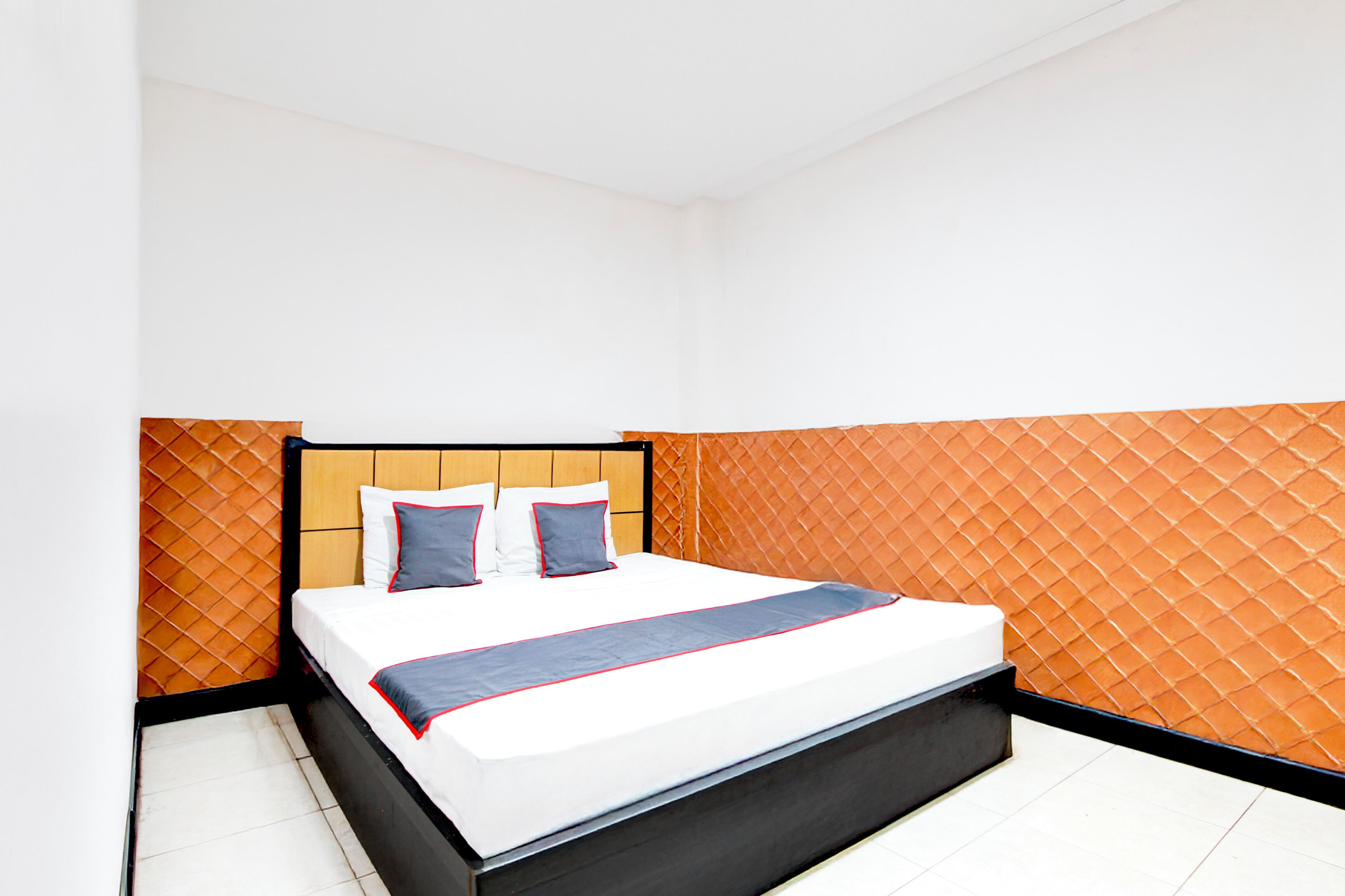 A modern hotel room with a large bed, a wooden headboard, and orange patterned walls.
