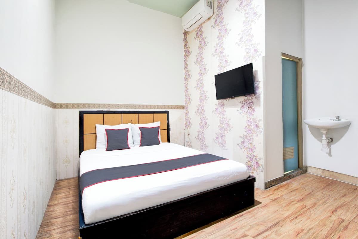 A hotel room with a bed, a TV mounted on the wall, a sink, and a door.