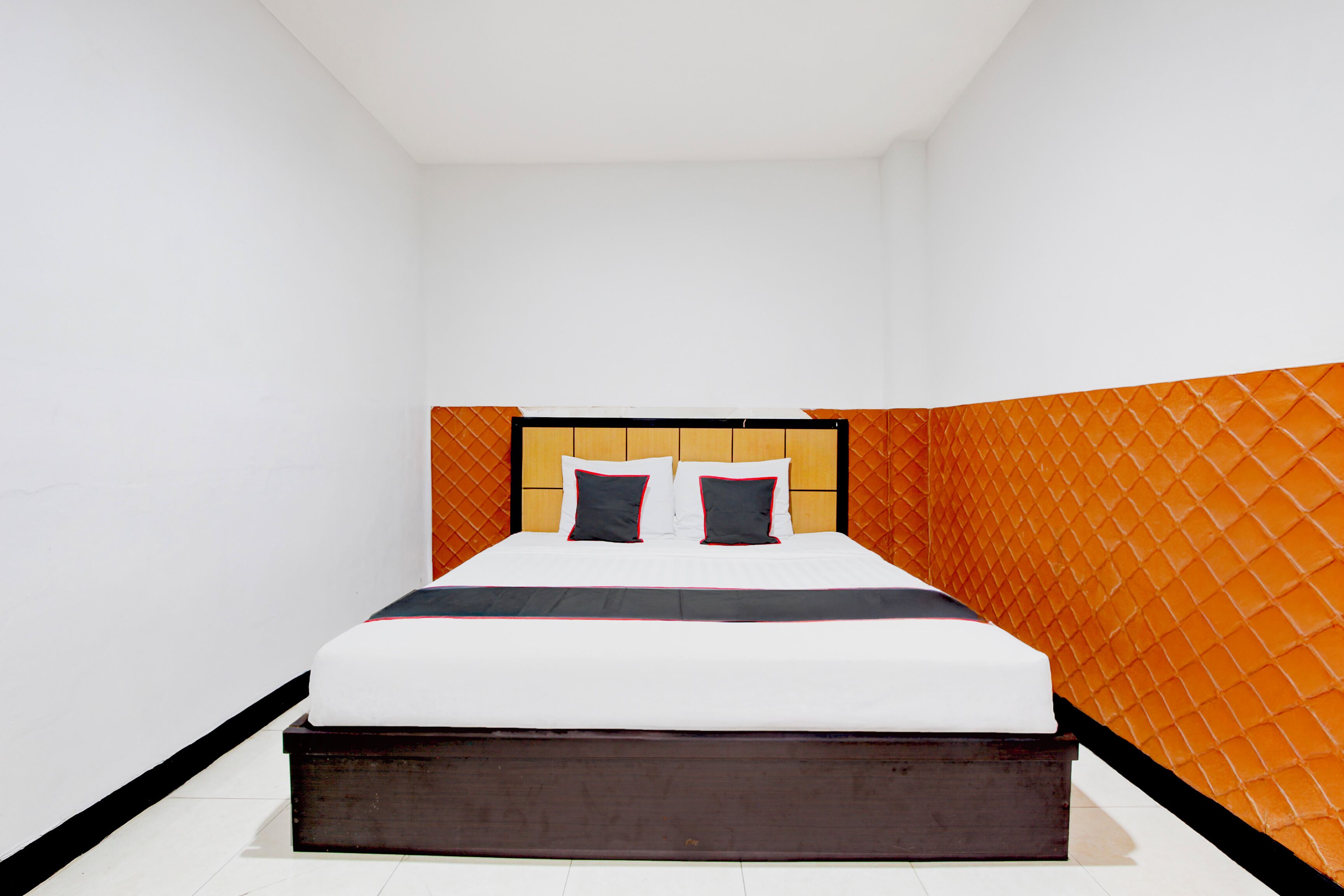 A neatly made bed with a wooden headboard and two pillows, set against a white wall with an orange accent wall.