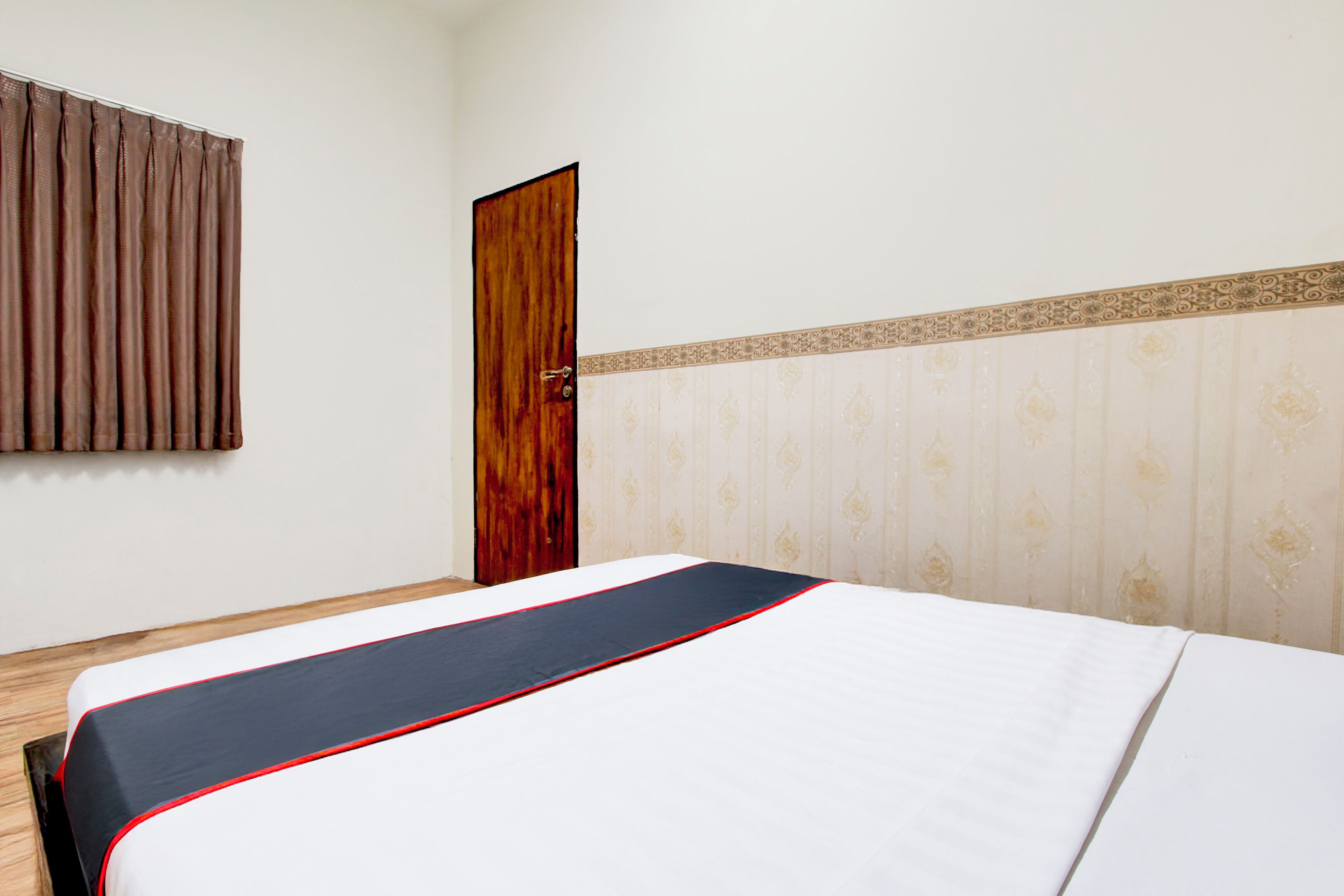 Une chambre d’hôtel avec un lit, une porte en bois et un rideau.