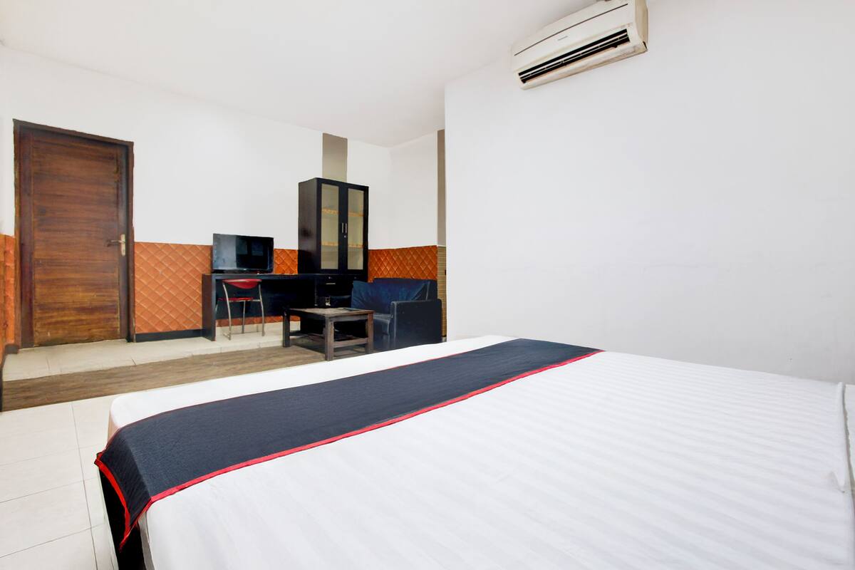 A hotel room with a bed, a desk, a chair, a television, and an air conditioning unit.