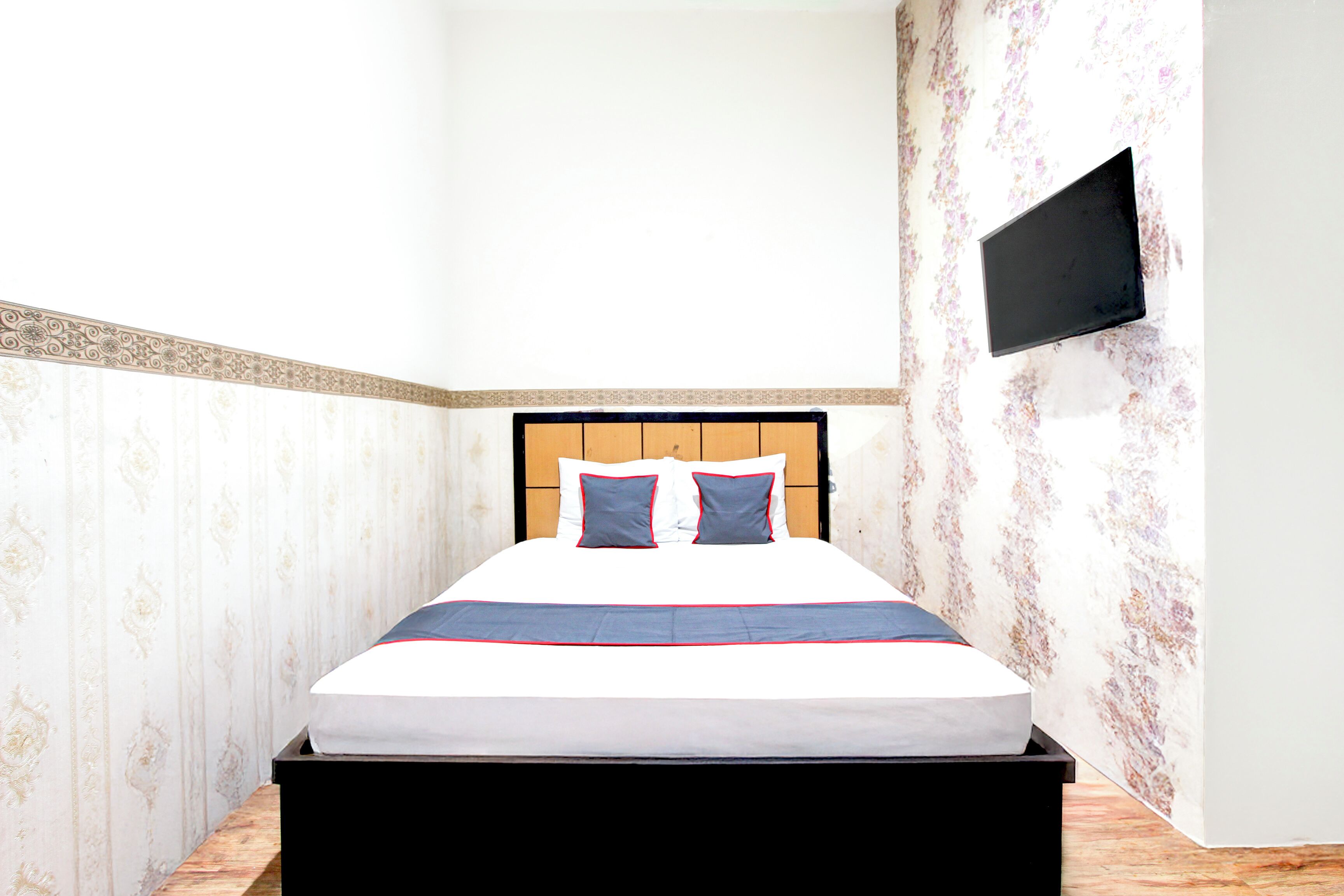 Un lit bien fait, avec une tête de lit, un téléviseur à écran plat fixé au mur et un papier peint à motifs.