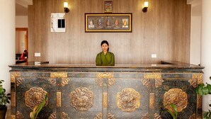 A reception desk with a woman standing behind it, framed artwork on the wall, and a wooden panel design. - Zhingkham Resort (Punakha)