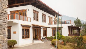 A two-story building with a restaurant sign, wooden balconies, and a garden area. - Zhingkham Resort (Punakha)