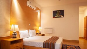 A hotel room with a bed, bedside tables, lamps, an air conditioner, a painting, and a patterned rug. - Zhingkham Resort (Punakha)