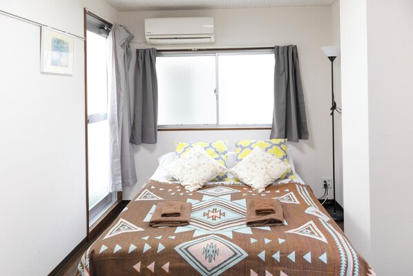 Una camera d'albergo con un letto grande, una finestra con tende, una lampada da terra e un condizionatore d'aria.