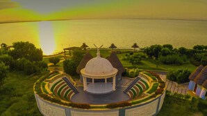 Um edifício circular com uma cúpula central e estruturas ao redor, rodeado por vegetação e um corpo de água.